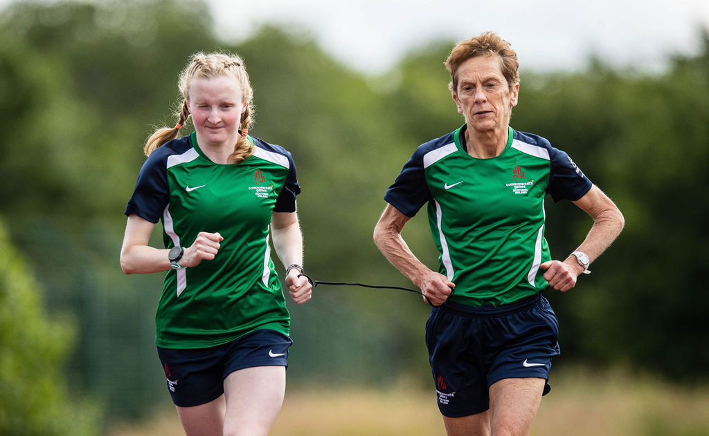 Judith MacCombe running with guide Anne Paul. They are wearing their Commonwealth Games training kit.